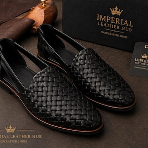 Pode incluir: Mocassins pretos de couro tecido com um perfil baixo e bico redondo. Os sapatos têm uma borda marrom contrastante e são exibidos com uma caixa de sapatos e uma etiqueta da Imperial Leather Hub.