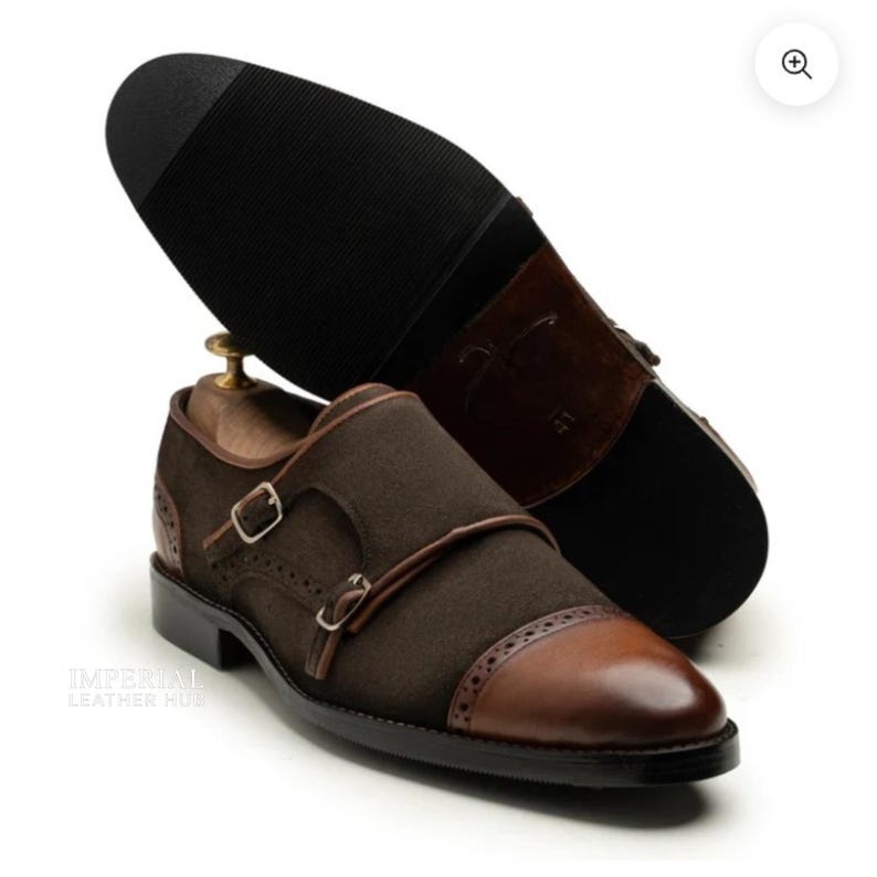 May include: Brown suede double monk strap dress shoes with leather accents. The shoes feature a cap toe design and two adjustable buckles. The sole is black, and the heel is brown. The shoes are displayed on a white background.