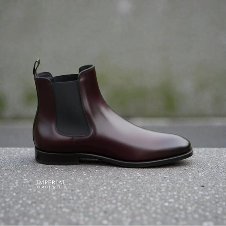 Pu&ograve; includere: Stivaletto Chelsea in pelle bordeaux lucida. Presenta un pannello laterale elastico nero e un tirante sul retro. La suola &egrave; nera. Il testo "IMPERIAL LEATHER HUB" &egrave; in basso. Design classico.