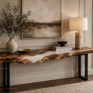 May include: A long console table featuring a natural live-edge wood slab top with a central white resin inlay, supported by two black metal U-shaped legs. The table surface holds a textured vase with greenery, a gold bowl, and a table lamp.