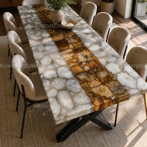 May include: A large rectangular dining table with a stone top. The table has a central band of brown and gold tones, surrounded by a white and grey pattern. The table is supported by a black metal base and surrounded by beige chairs.