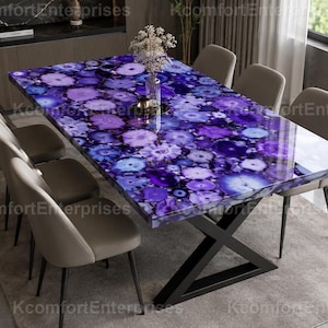May include: A rectangular dining table featuring a polished surface made of purple and blue agate slices, supported by a black metal X-shaped base. Six upholstered chairs in a neutral beige colour are arranged around the table.