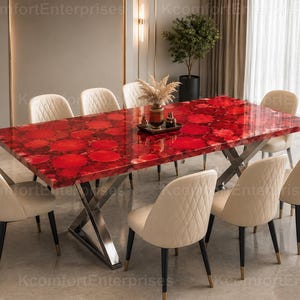 May include: A rectangular dining table with a polished red agate stone top featuring circular patterns and a metallic silver X-shaped base. The table is surrounded by eight cream-coloured upholstered chairs with diamond-stitched backrests.
