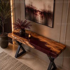 Op de afbeelding: Een rechthoekige sidetable met een natuurlijk houten blad met boomranden en een dieprode harsinleg. De tafel wordt ondersteund door twee zwarte, X-vormige metalen poten. Op het blad staan een donkere vaas met rood blad en een kleine kaars.