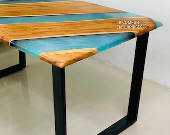 Può includere: Un tavolo in legno dal design unico. Il piano del tavolo presenta fasce alternate di legno marrone chiaro e resina blu traslucida. Il tavolo ha gambe in metallo nero. Il testo "K COMFORT ENTERPRISES" è visibile sul bordo del tavolo.