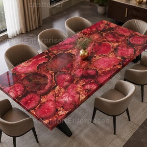 May include: A rectangular dining table featuring a polished surface composed of vibrant red and deep crimson agate stone slices, supported by a black metal base, surrounded by six beige upholstered chairs with curved backrests.
