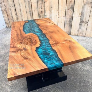 Könnte beinhalten: Holz-Couchtisch mit einem Fluss aus türkisfarbenem Kunstharz in der Mitte. Der Tisch hat eine natürliche Holzmaserung und steht auf einem schwarzen Sockel. Der Text "K COMFORT ENTERPRISES" ist sichtbar.