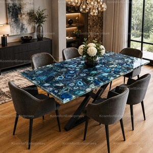 Könnte beinhalten: Rechteckiger Esstisch mit blauer Achatsteinplatte und schwarzem Metallgestell. Sechs graue, gepolsterte Stühle umgeben den Tisch. Der Raum hat Holzböden und ein modernes Design. Der Tisch ist etwa 200 cm lang.