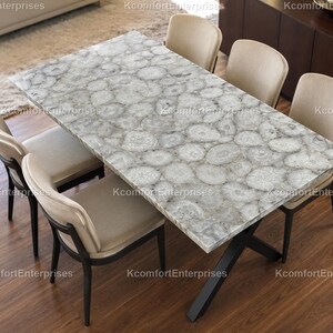 May include: A rectangular dining table with a grey and white agate stone top. The table has a black metal base. Six beige upholstered chairs with black legs surround the table, creating a modern dining set.