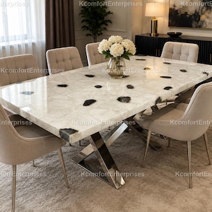 May include: A contemporary dining table with a white quartz surface featuring black inlays. It is supported by a polished chrome base and surrounded by eight beige upholstered chairs. A vase of white flowers is on the table.