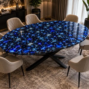 May include: An oval dining table featuring a polished blue agate gemstone surface with a vibrant, multi-tonal blue mosaic pattern, supported by a black metal X-shaped base, surrounded by six beige upholstered chairs with vertical stitching.