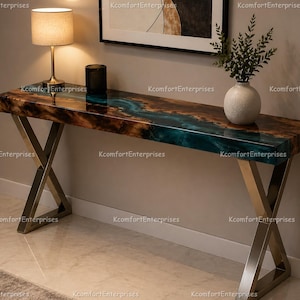 May include: A modern console table with a live edge wooden top featuring a teal epoxy river. The table has a polished metal X-shaped base and is accented with a small lamp and a decorative vase.
