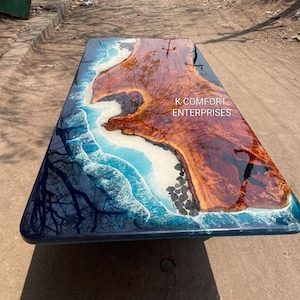 May include: A rectangular wooden table with a glossy resin finish. The table features a natural wood grain center, surrounded by a blue and white wave design. The text "K COMFORT ENTERPRISES" is visible on the table's surface.
