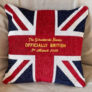 Pode incluir: Almofada quadrada com o design da bandeira Union Jack em vermelho, branco e azul marinho. O centro da almofada tem um texto bordado a ouro: "The Schwiderski Family OFFICIALLY BRITISH 5th March 2026."