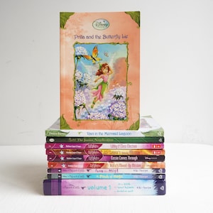 May include: A stack of Disney Fairies books. The top book is titled "Prilla and the Butterfly Lie" with a fairy and butterfly illustration. Other titles include "Rani in the Mermaid Lagoon" and "The Junior Novelization". The books are in various colors.