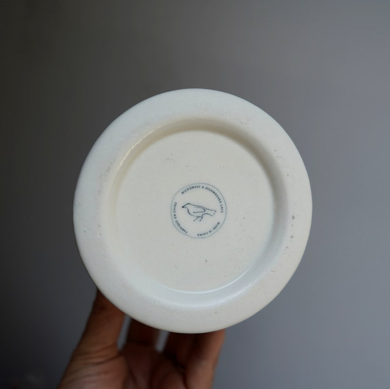 Pu&ograve; includere: Tazza in ceramica bianca con un logo di uccello bianco e nero che recita "Microwave & Dishwasher Safe. Made in China. Crafted for the Home."