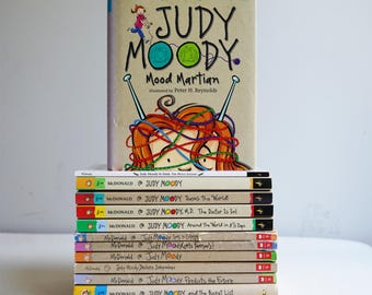 May include: A stack of Judy Moody children's books by Megan McDonald. The top book is titled Judy Moody Mood Martian, featuring a cartoon character with tangled yarn on the cover. Below it are several other books in the series with spines visible.