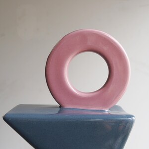 May include: A contemporary ceramic sculpture with a pink circular element on a blue geometric base. The sculpture has a glossy finish and a minimalist design, suitable for home decor.
