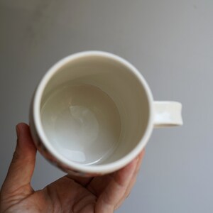 Pu&ograve; includere: Una tazza in ceramica bianca con un manico. La tazza &egrave; vuota e l'interno &egrave; visibile.
