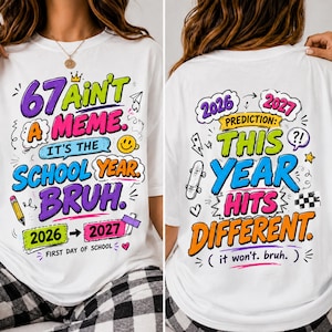 以下が含まれることがあります： カラフルなグラフィックテキストとイラストが特徴の白いTシャツ。前面には「67 AINT A MEME. IT'S THE SCHOOL YEAR. BRUH. 2026-2027 FIRST DAY OF SCHOOL」とあり、背面には「2026 2027 PREDICTION: THIS YEAR HITS DIFFERENT (it won't. bruh.)」とプリントされています。