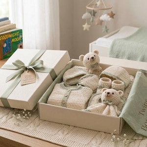 Può includere: Una scatola regalo contenente un set per neonati all'uncinetto color crema con dettagli verde salvia. Il set include un cardigan abbottonato, due berretti, due scarpine e due orsetti all'uncinetto. La scatola è chiusa da un nastro verde salvia.