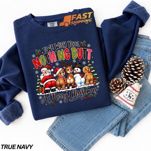 Puede incluir: Una sudadera azul marino de cuello redondo con un gráfico de Santa Claus, un oso, un reno, un muñeco de nieve y un hombre de jengibre, con el texto "WE WISH YOU NOTHING BUTT A MERRY CHRISTMAS" rodeado de copos de nieve, acebo y pinos.