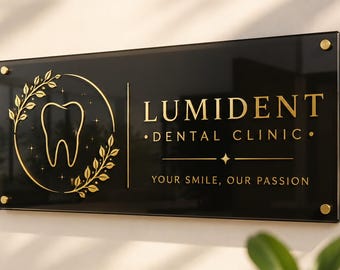 May include: A rectangular black sign with gold lettering and accents mounted on a wall. The sign features a central tooth icon inside a circular laurel wreath, with the text LUMIDENT DENTAL CLINIC and the slogan YOUR SMILE, OUR PASSION.