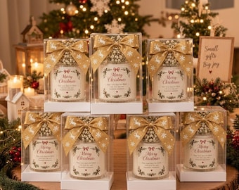 May include: Seven glass candles in clear boxes, each topped with a gold ribbon featuring white reindeer and snowflakes. The labels read Merry Christmas with a decorative wreath design. The candles are arranged on a wooden surface.