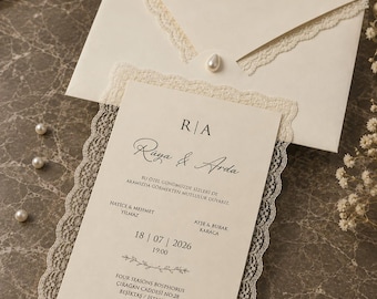 May include: An off-white wedding invitation card and matching envelope, both featuring delicate cream-colored lace trim. The card displays the names Rüya & Arda, event details, and a small pearl accent on the envelope flap, presented with scattered pearls.