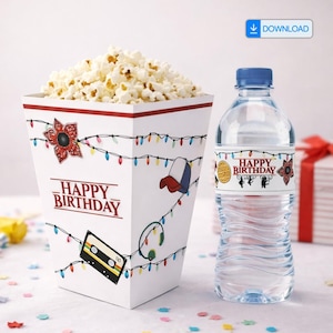 Peut inclure: Un seau à pop-corn blanc rempli de pop-corn, décoré d'une fleur de Demogorgon rouge et noire, d'une casquette de baseball et de guirlandes lumineuses. Une bouteille d'eau avec une étiquette assortie qui dit "Happy Birthday" est à côté du récipient.