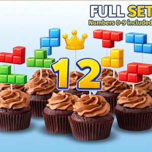 May include: Cupcakes with chocolate frosting, topped with colorful game-themed decorations and the number 12. The image also includes a gold crown and the text "FULL SET Numbers 0-9 included!"