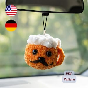 May include: A crocheted beer mug ornament hanging from a black cord. The mug is orange with a white foam top, featuring two large black plastic eyes, a black plastic nose, and a stitched black mustache. The text PDF Pattern is visible.