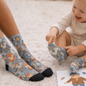 Peut inclure: Chaussettes bleues ornées d'animaux de la forêt, comme des renards et des loups. Les chaussettes ont des talons et des orteils noirs. Un enfant porte une chaussette assortie et joue avec une image d'une personne.