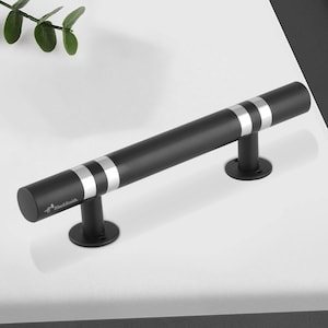 以下が含まれることがあります： シルバーのアクセントリングが付いた黒いキャビネットプル。円筒形のハンドルは、2つの円形のベースに取り付けられています。「BlackSmith」の文字がハンドルの左端に印刷されています。モダンな美学のために設計されたハードウェアです。