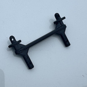 May include: A black, 3D-printed object with a unique geometric design. The object has a central bar with textured detailing, connecting two angled supports. Each support features a hole and a cross-shaped element.
