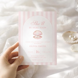 May include: A pink and white striped baby shower invitation with the text "She'll Be Here Soon." The invitation features a seashell graphic with pearls and event details. The date is August 16.