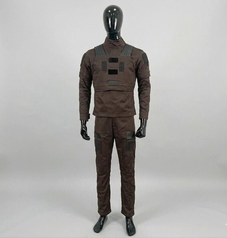 May include: A dark brown tactical uniform set consisting of a long-sleeved shirt with a high collar and matching trousers. The shirt features black rectangular patches on the chest and shoulders, while the trousers include black knee panels.