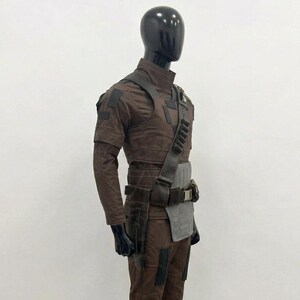 May include: A brown tactical costume set worn on a black mannequin, featuring a high-neck long-sleeve shirt, matching trousers, a dark brown shoulder strap with ammunition loops, and a grey rectangular hip panel with a utility belt and holster.