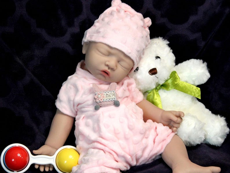 A baby doll holding a pacifier, next to a plush stuffed animal, set against a pastel background.