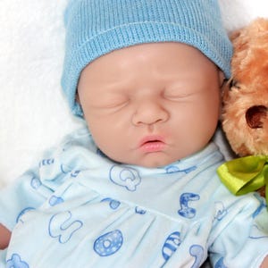 A baby doll resting on a soft purple blanket, showcasing its delicate features and clothing.