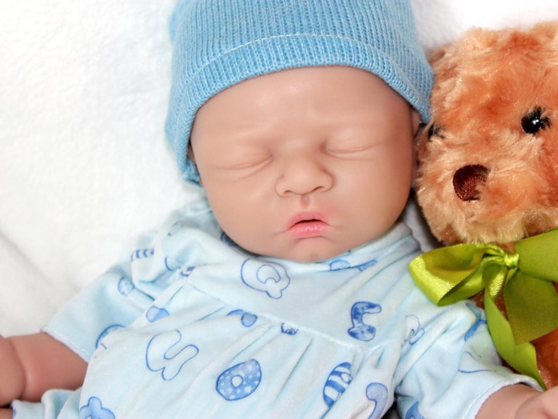 A baby doll resting on a soft purple blanket, showcasing its delicate features and clothing.