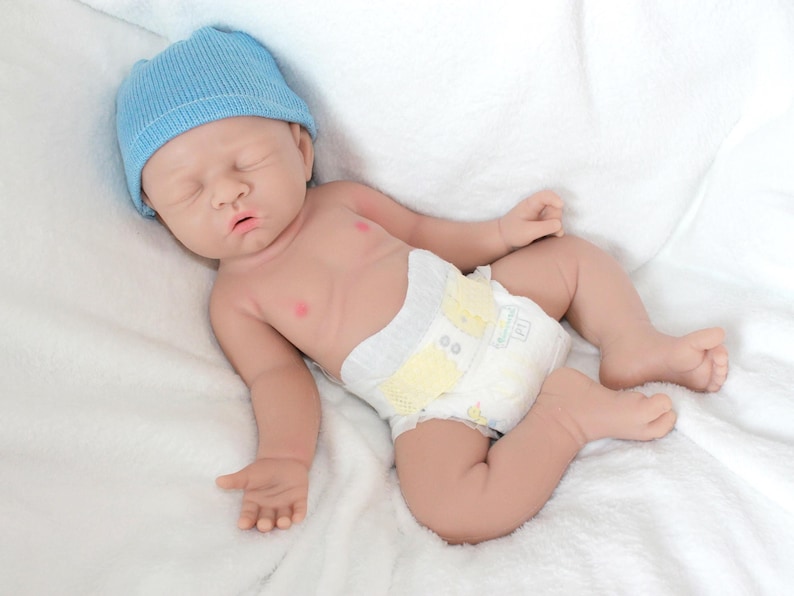 A baby doll resting on a soft purple blanket, showcasing its delicate features and clothing.
