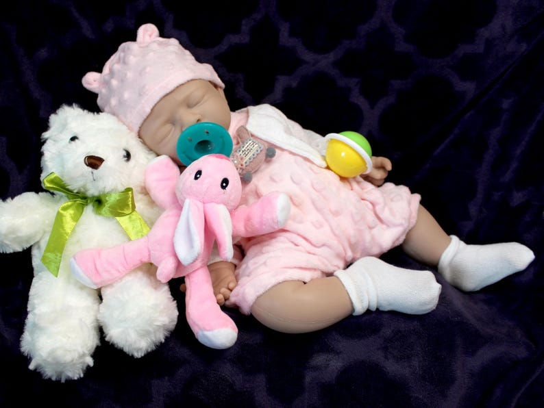 A baby doll resting on a soft purple blanket, showcasing its delicate features and clothing.