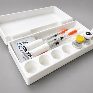 Può includere: Un contenitore organizzatore in plastica bianca contenente due siringhe trasparenti con tappi arancioni, due bobine bianche contrassegnate con CR, una salvietta imbevuta di alcol e tre piccole fiale di vetro con tappi gialli e bianchi marcati CR.