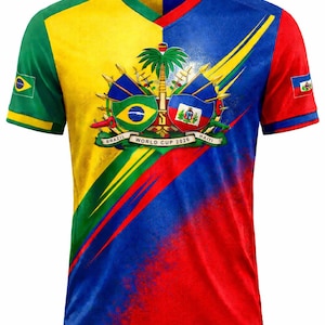 May include: A V-neck t-shirt with a split design featuring the flags of Brazil and Haiti. The shirt has a yellow, green, blue, and red color scheme with the text "WORLD CUP 2026". The shirt also has the flags of Brazil and Haiti.