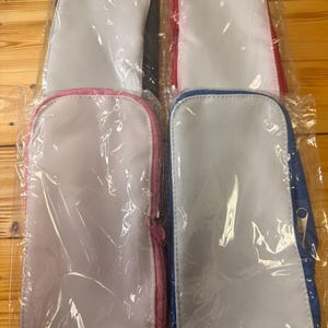 May include: Four rectangular pouches in clear plastic packaging. The pouches have a white center and colored trim in black, red, pink, and blue. Each pouch has a zipper closure. The pouches are likely for storing small items.