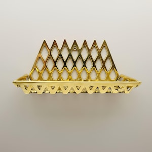 Op de afbeelding: Een goudkleurig, decoratief wandrek met een geometrisch ruitpatroon. Het rek heeft een rechthoekige basis en een driehoekige bovenkant, met een klein gat om op te hangen. Het ontwerp is sierlijk en gedetailleerd.