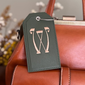 May include: A green leather luggage tag with a pink embroidered letter "W" on it.