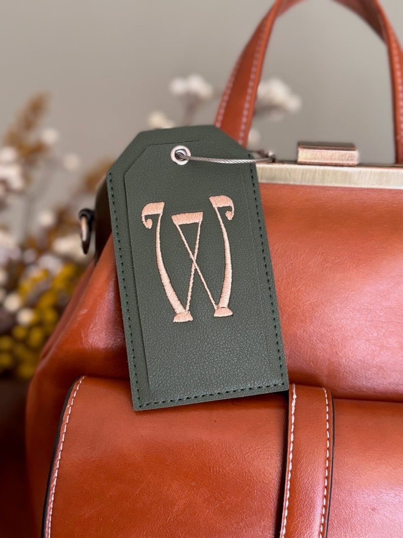 May include: A green leather luggage tag with a pink embroidered letter "W" on it.