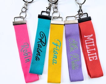 May include: Five colorful keychains with embroidered names. The keychains are pink, teal, yellow, purple, and red. Each keychain has a different name embroidered in a contrasting color: Robin, Raina, Fiona, Mia Willis, and Millie.